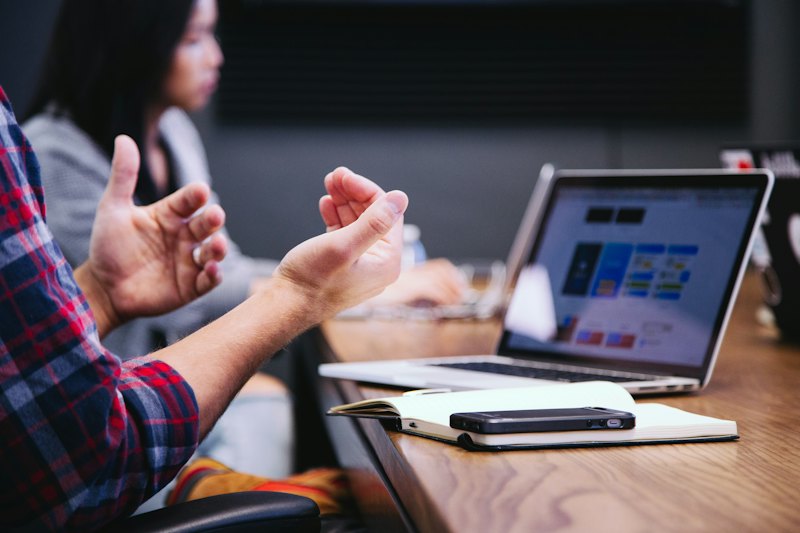 Person gesturing while talking at a meeting table with laptops